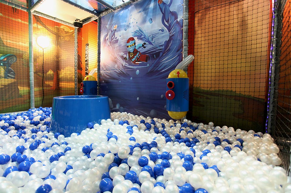 Indoor play area featuring a colourful ball pit filled with blue and white balls, surrounded by vibrant walls and playful decorations.