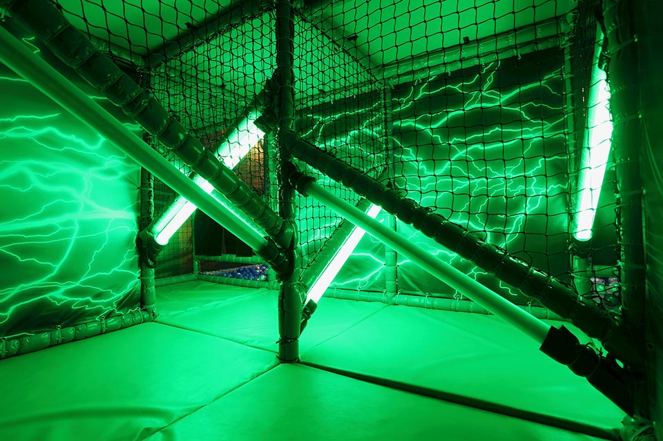 Interior view of a vibrant green play area featuring illuminated tubes and a netted structure, designed for children's entertainment and adventure activities.