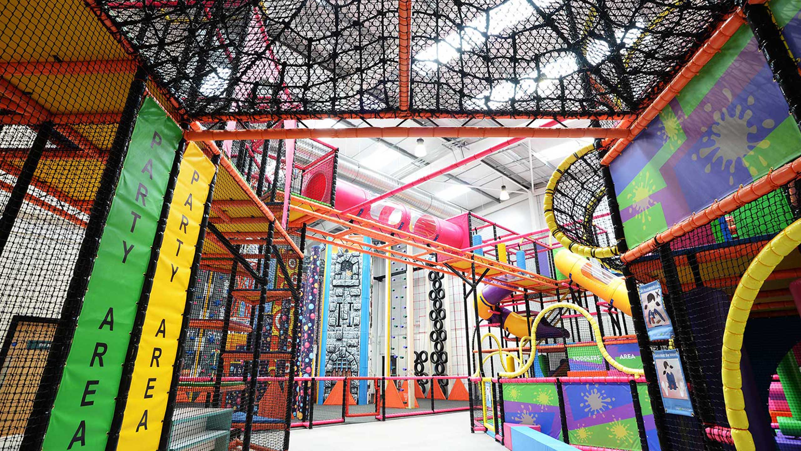 Indoor adventure playground featuring vibrant climbing structures, slides, and obstacle courses designed for children. The facility is brightly coloured and offers a safe environment for active play and exploration.