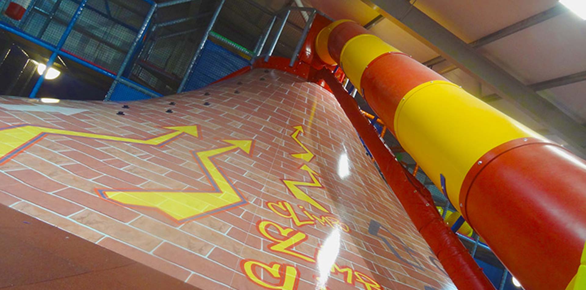 Indoor play area featuring a brightly coloured slide and textured climbing surface, designed for children's entertainment and physical activity.