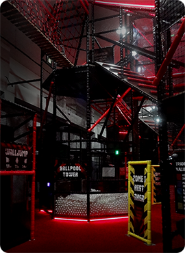 Indoor adventure park featuring climbing structures, ball pit, and various play zones, illuminated with red lighting for an exciting atmosphere.