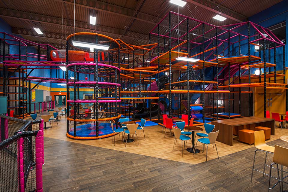 Indoor play area featuring a multi-level climbing structure with vibrant colours, seating areas, and a spacious layout designed for children's entertainment and activities.