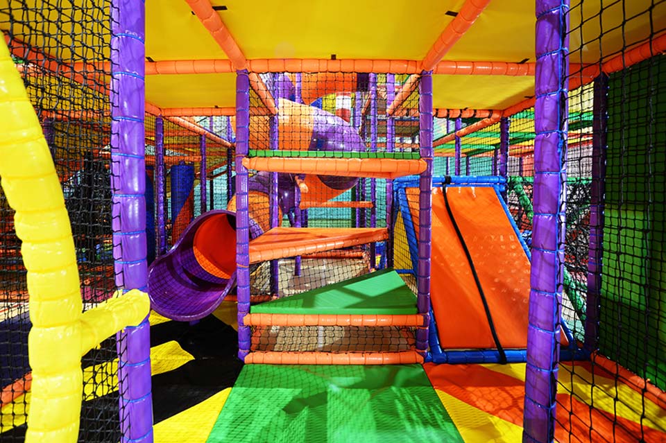 Brightly coloured indoor play area featuring multiple climbing structures, slides, and tunnels designed for children's entertainment and physical activity.