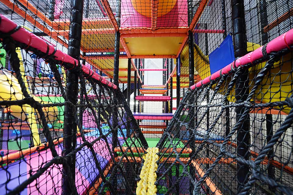 Colourful indoor play area featuring multi-level climbing frames and netted walkways, designed for children's entertainment and physical activity.