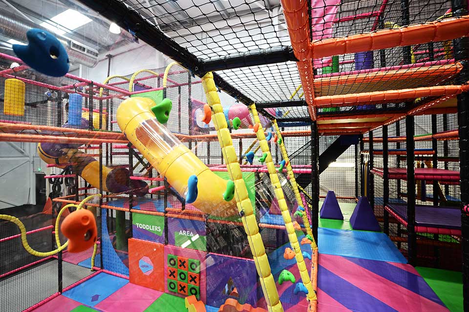 Indoor adventure playground featuring colourful climbing structures, slides, and soft play areas for children. The vibrant layout encourages active play and exploration in a safe environment.